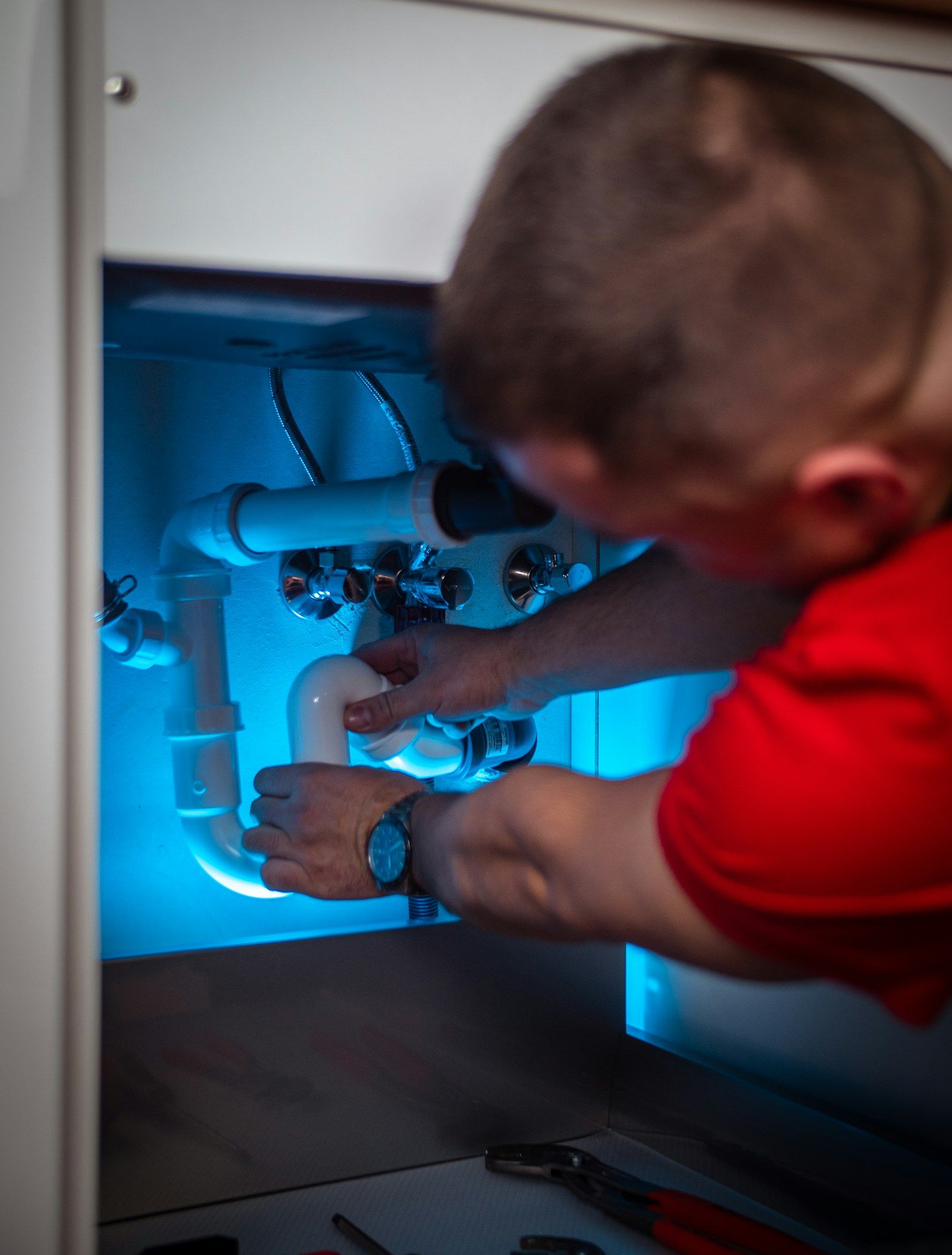 Plumber clearing a drain line under a kitchen sink cabinet